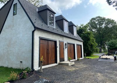 A small white building with wooden doors, a shingled roof, and black gutters