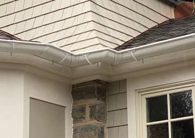 A beige building with a gray shingled roof and white gutters