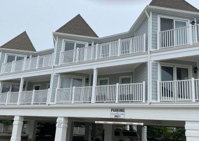 A parking lot under a grey lodge building. There are white fences on each balcony and white gutters