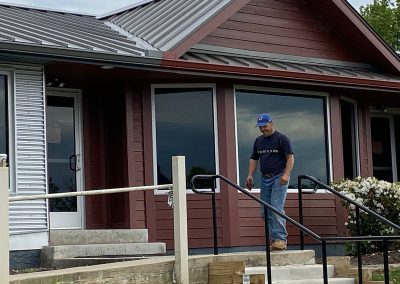 A man in front of a building with mahogany siding, a metal roof, and mahogany gutters