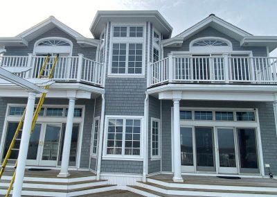 A large gray building with white trim and white gutters. There's a yellow ladder leaning against a balcony