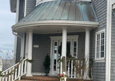 White gutters running along a porch roof. The porch is brick and decorated with potted plants