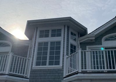 The sun setting behind the top half of a grey building with white gutters