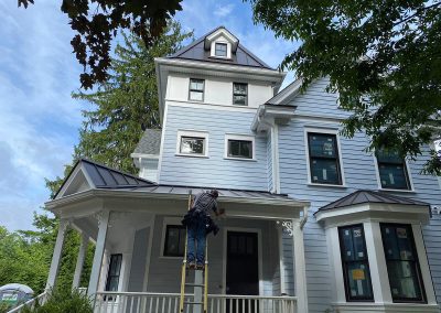 A figure on a ladder installing gutters on a large blue house