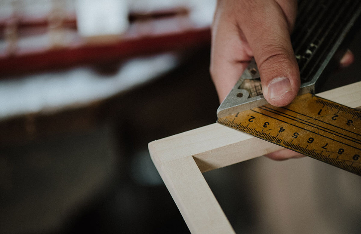 A hand holding a measuring tool to a wooden frame