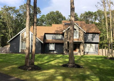 A blue-grey house with brown shingles in front of a forest