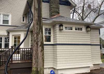 A beige house with white gutters. The gutters are being drained by a long black hose