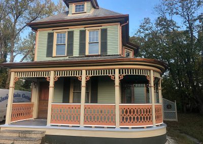 A green house with a wraparound porch and bronze gutters