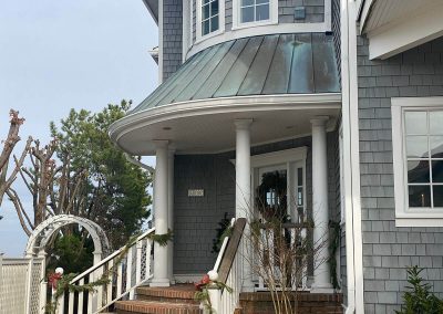 A weathered blue-grey building with a brick porch and white gutters