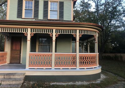 A two-story green house with a wraparound porch