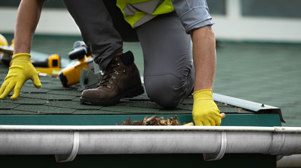 male contractor cleaning clogged roof gutter